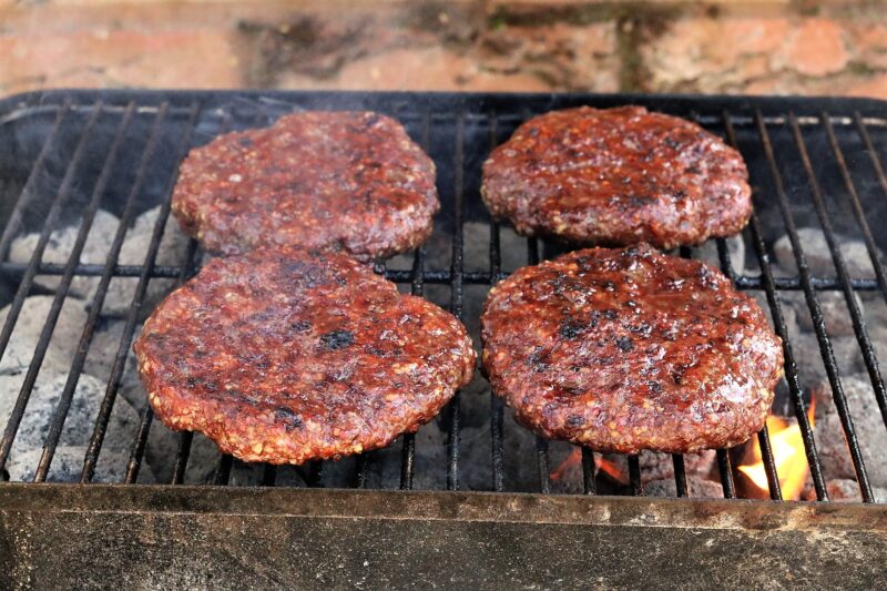 Hand-made burgers sizzling on a BBQ.