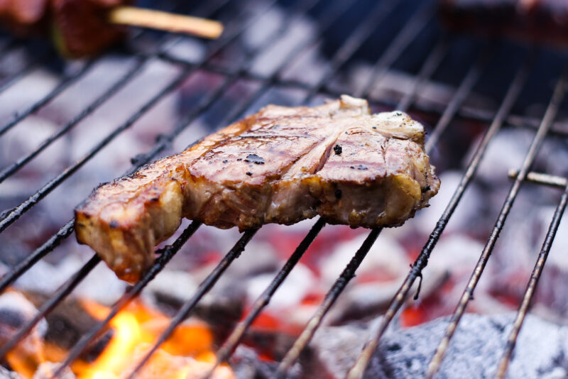 Pork steak cooking on a BBQ.